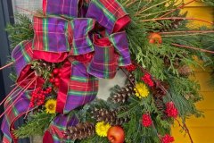 Mixed green wreath with multi-color plaid and red backed bow. Dried flowers, fruit, berries and pine cones.